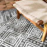 Close up of Frankville Black&White All Over Performance Rug with geometric pattern under a woven chair. Styleshot