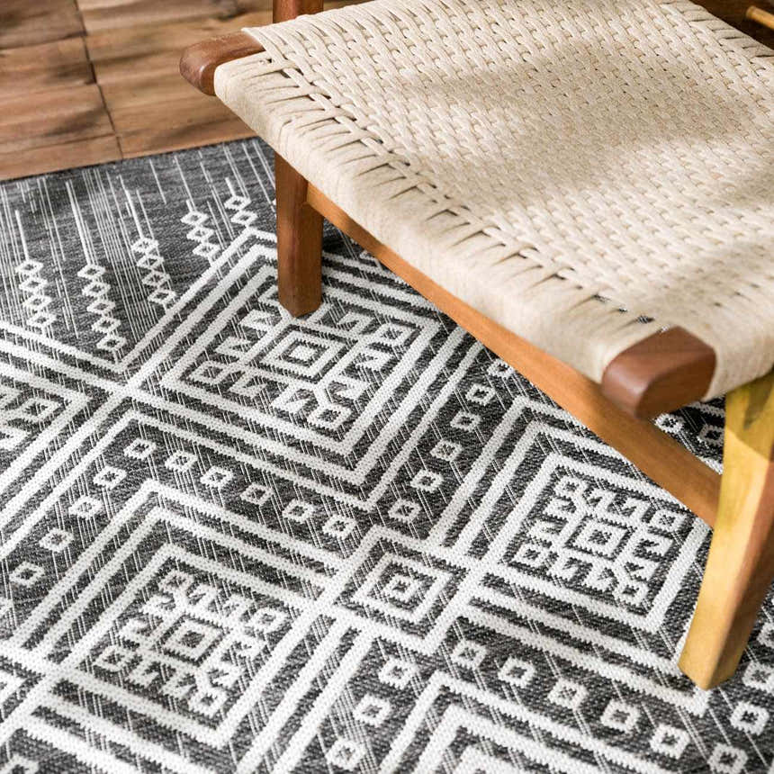 Close up of Frankville Black&White All Over Performance Rug with geometric pattern under a woven chair. Styleshot