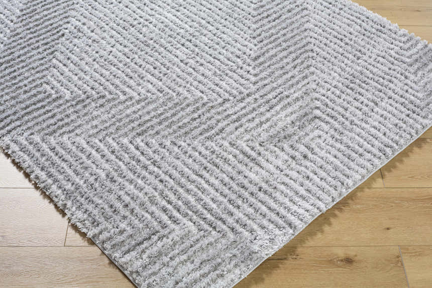 Close-up of the Ashlyn Gray Area Rug showing its shag texture and contemporary chevron pattern on wood floor. Corner
