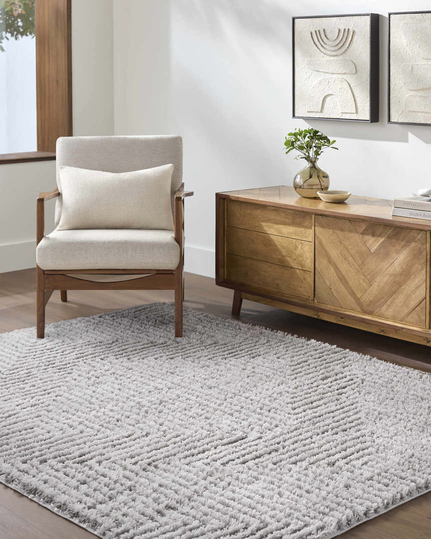 Living room scene with a light slate Ashlyn Area Rug, beige chair, and wood cabinet with abstract art. Roomscene-Rectangle