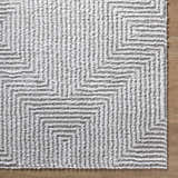 Close-up of the Ashlyn Light Slate Area Rug. Gray and white shag rug with a geometric pattern. Soft, textured rug on wood floor. Corner