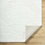 Close-up of the plush, cream Ashlyn White Area Rug featuring a subtle geometric shag design on light wood floors. Fold