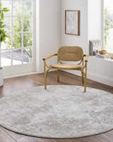Bright room scene with a round, beige Ganit Thick Luxe Boutique Rug under a woven chair. Roomscene-Round