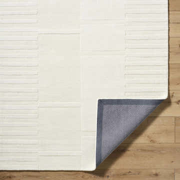 Close-up of Alisha Area Rug. Ash and light silver wool rug with geometric pattern and hand-loomed texture. Fold