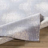 Close-up of the Simpatico Candice Olson x LIVABLISS area rug. Machine woven wool rug in cream, gray, and light blue on wood floor. Fold