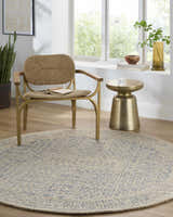 Sunlit room with a round Hinton Wool Area Rug, woven chair, and gold side table. Serene, neutral tones. Roomscene-Round