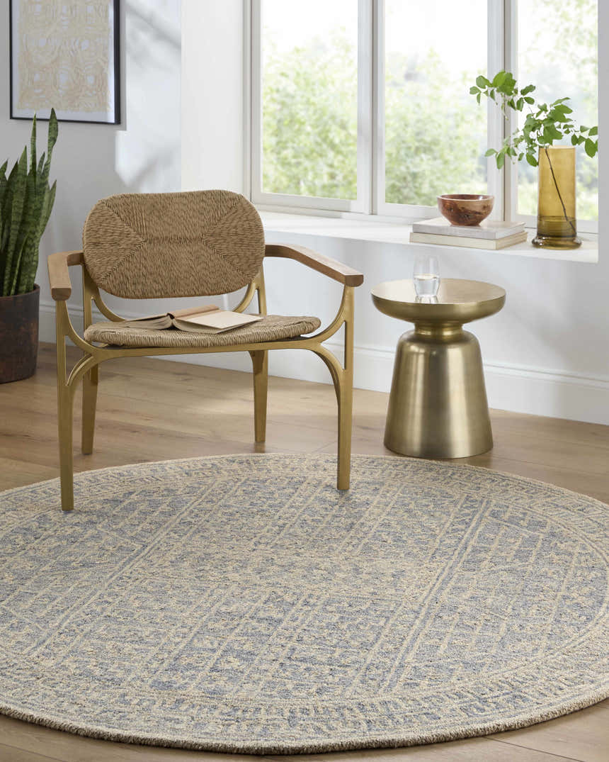 Sunlit room with a round Hinton Wool Area Rug, woven chair, and gold side table. Serene, neutral tones. Roomscene-Round
