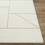 Close-up of the ivory Alaina Area Rug, a hand-tufted wool rug with a charcoal geometric pattern on a wood floor. Front