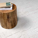 Close-up of the cream Andia Plush Grid Rug with a subtle geometric pattern and a rustic wood side table. Styleshot