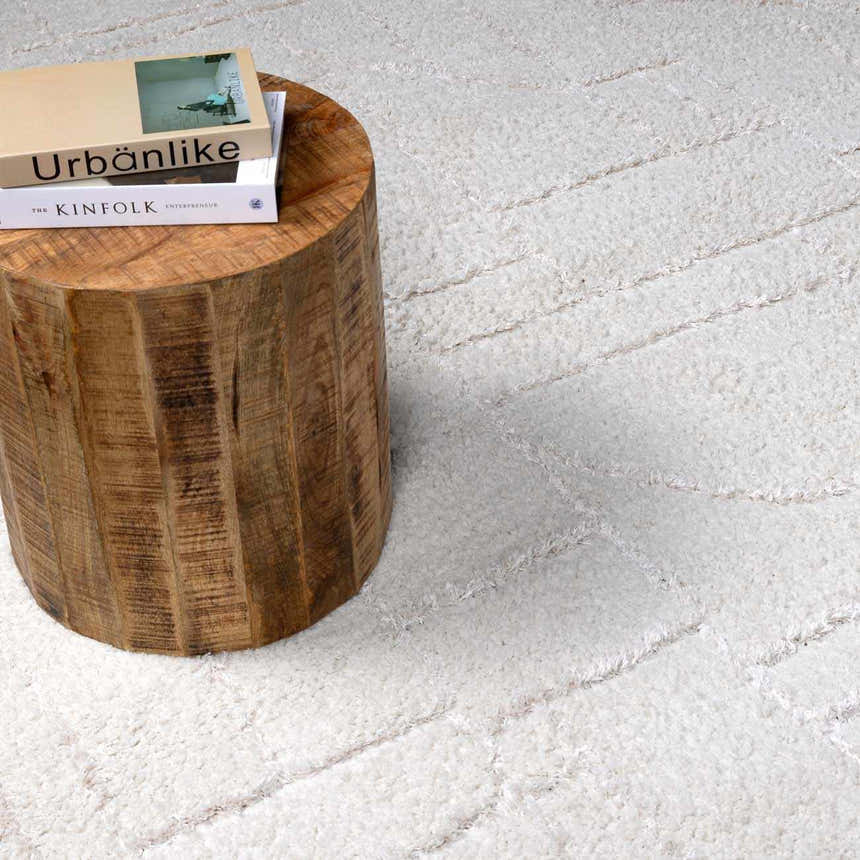 Close-up of the cream Andia Plush Grid Rug with a subtle geometric pattern and a rustic wood side table. Styleshot