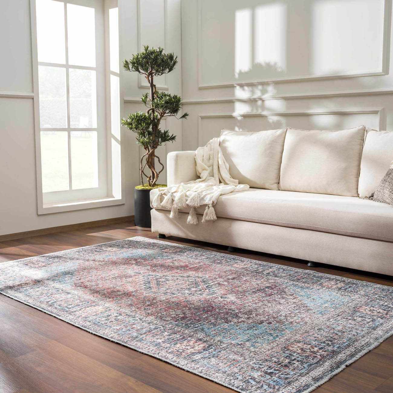 Living room scene with a Blue Burgundy Holi-2302 rug, cream sofa, wood floors, and natural light from a large window. Roomscene-Rectangle