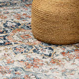 Close up of the Dorval Traditional Rug showing brick red, cream, and blue oriental pattern with a jute pouf. Styleshot