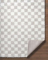 Close-up of the Ardice Area Rug, a shag rug with an ivory and peach checkerboard pattern on hardwood floors. Fold