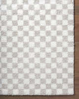 Close-up of the Ardice Area Rug, a shag rug with an ivory and peach checkerboard pattern on wood flooring. Corner