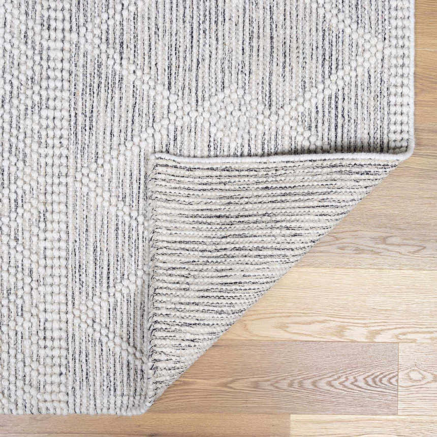 Close-up of the hand woven New Whittington Area Rug. Gray and off-white geometric pattern with a textured wool feel. Fold