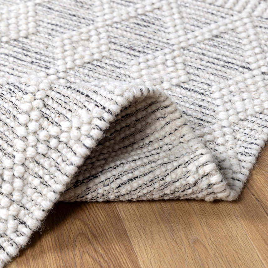 Close-up of the hand-woven New Whittington Area Rug. Gray and off-white geometric pattern with a looped, textured wool pile. Fold