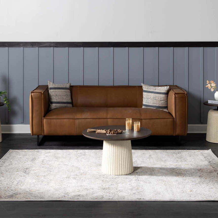 Living room scene with a brown leather sofa and beige Parkerfield Area Rug. Roomscene-Rectangle