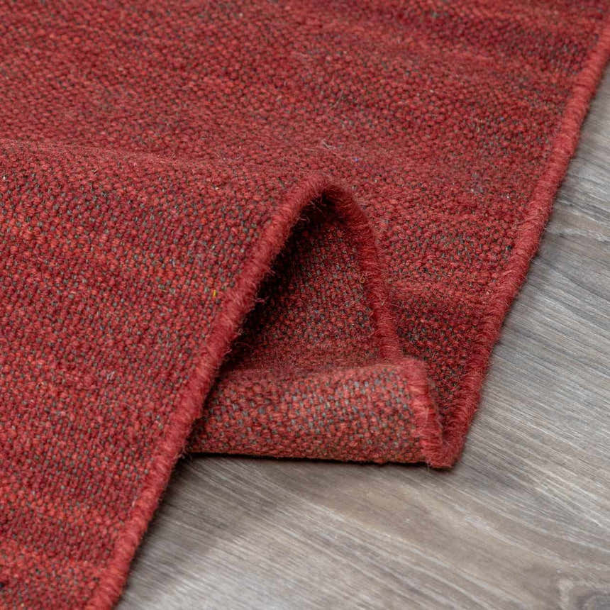 Close-up of the brick red Hedon Wool Area Rug showing its hand woven texture and wool material. Fold