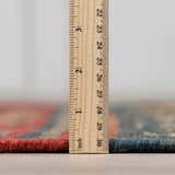 Close up of the pile height of the Hedon Wool Area Rug in brick red and navy with a ruler for scale. Pile