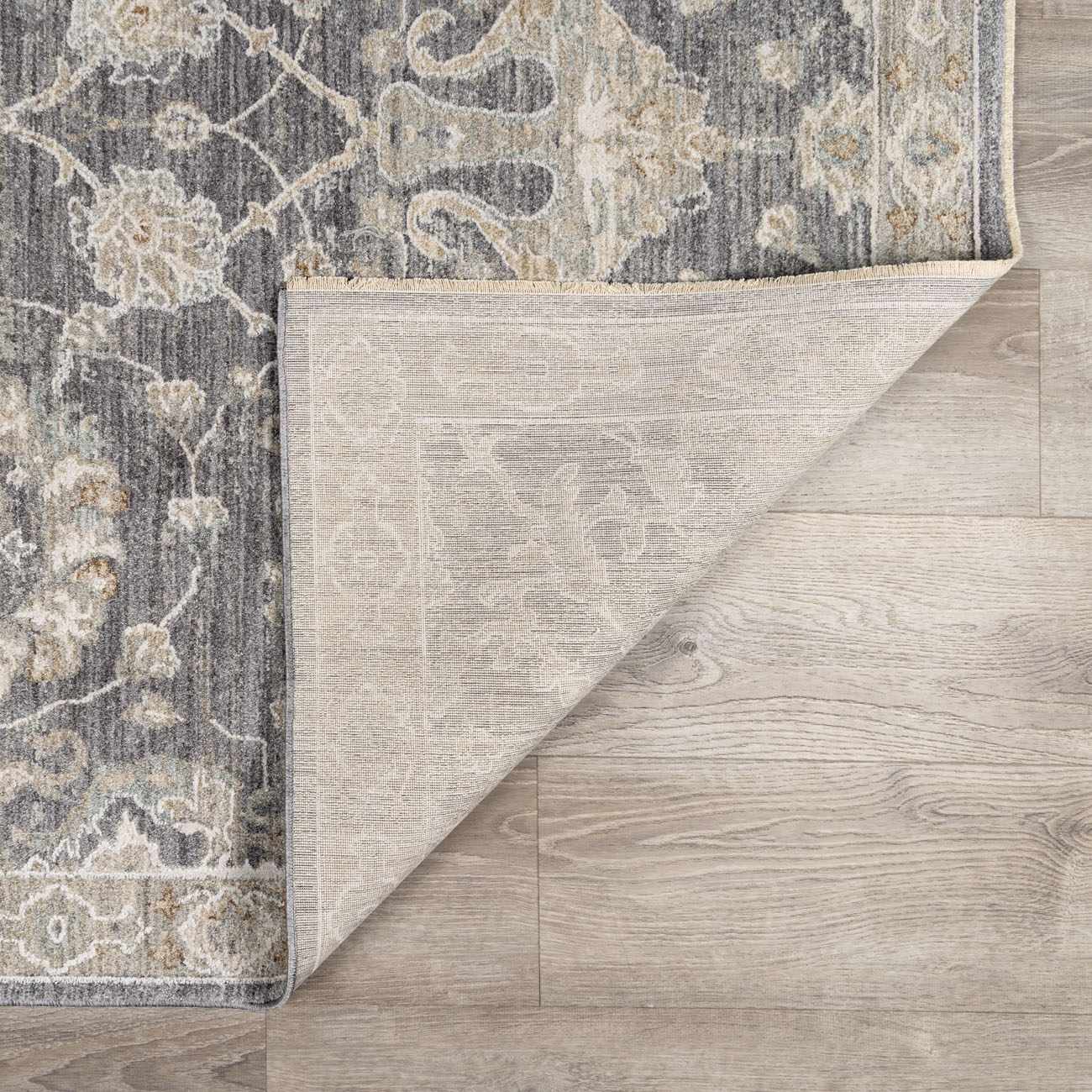 Close up of the Kanimbla Thick Luxe Avant Garde Rug showing its gray, beige, and floral pattern and woven backing. Fold