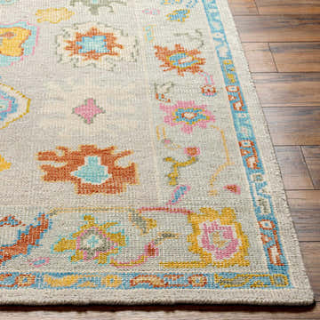 Close-up of the Kapaya Premium Wool Rug showing its floral pattern, brick red, aqua, yellow, and pink colors. Hand-knotted texture. Front