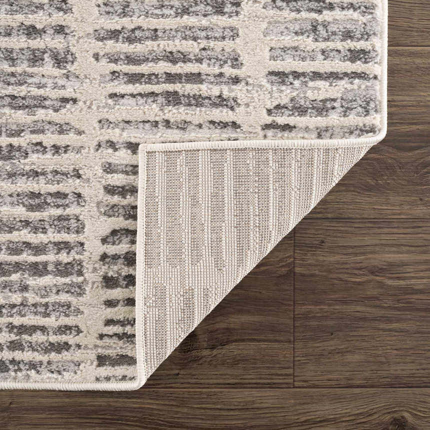 Close up of the Aricin Gray Area Rug showing light silver and gray stripes on dark wood floor. Fold