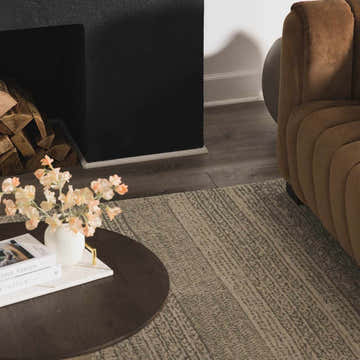 Living room scene with a brown velvet chair and the Kinmundy Tufted Maroc Wool Rug in gray and ivory by a fireplace. Roomscene-Rectangle