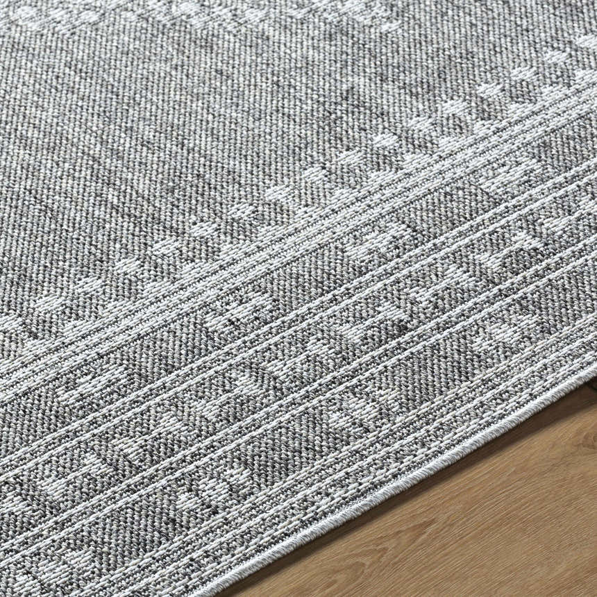 Close-up of the Asuman Area Rug. Gray and white rug with a traditional geometric pattern and woven texture. Texture