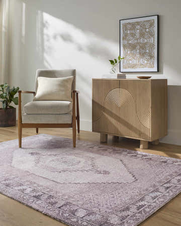 Living room scene with a traditional Wayde Area Rug in dusty rose, gray chair, and light wood cabinet. Roomscene-Rectangle