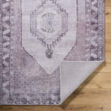Close-up of the hand-tufted Wayde Area Rug. Traditional design in dusty rose, lavender, and mauve on a wood floor. Fold