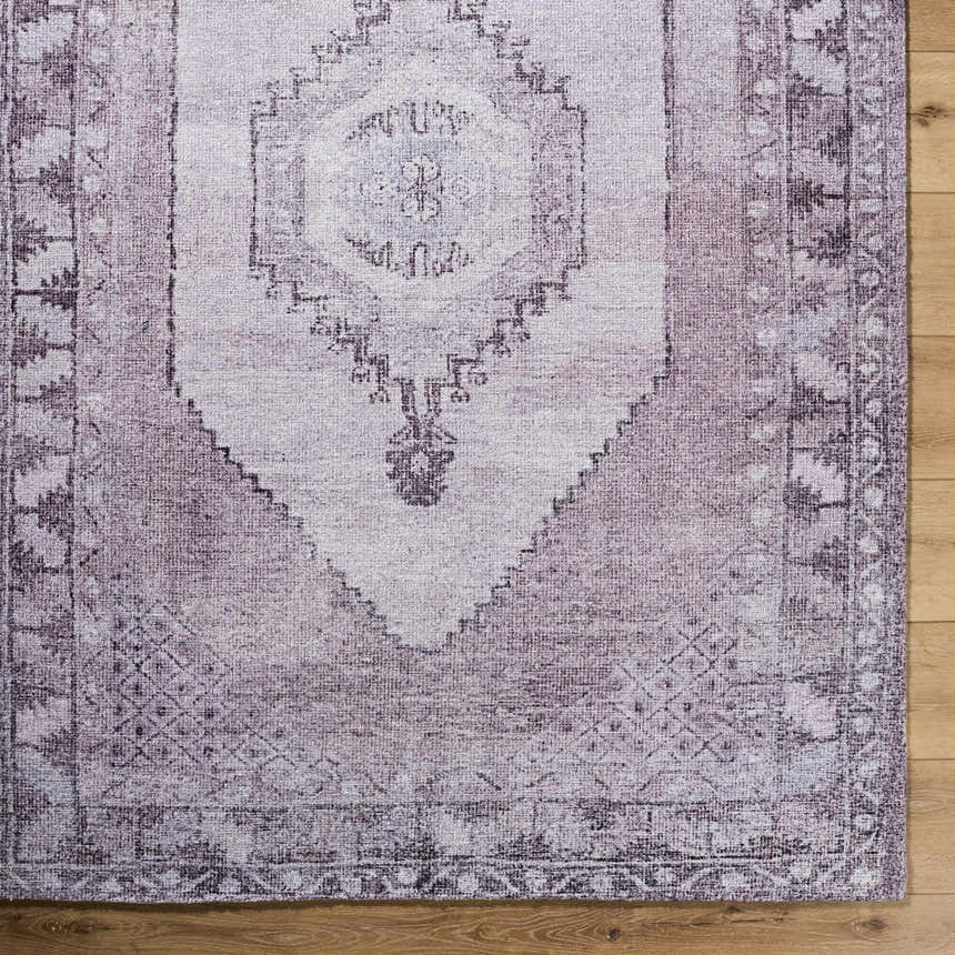 Close up of the Wayde Area Rug. Traditional rug with dusty rose, lavender, and mauve hues on a wood floor. Corner