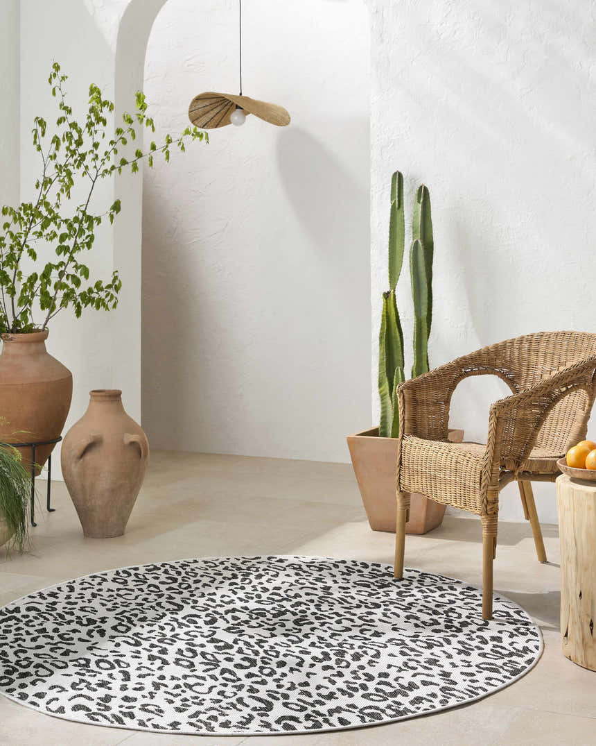 Sunlit patio with round Alderbury White Leopard Print Rug, wicker chair, terracotta pots, and neutral tones. Roomscene-Round