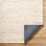 Close-up of the hand-tufted Winta Beige Wool Area Rug showing texture and backing on a wood floor. Fold