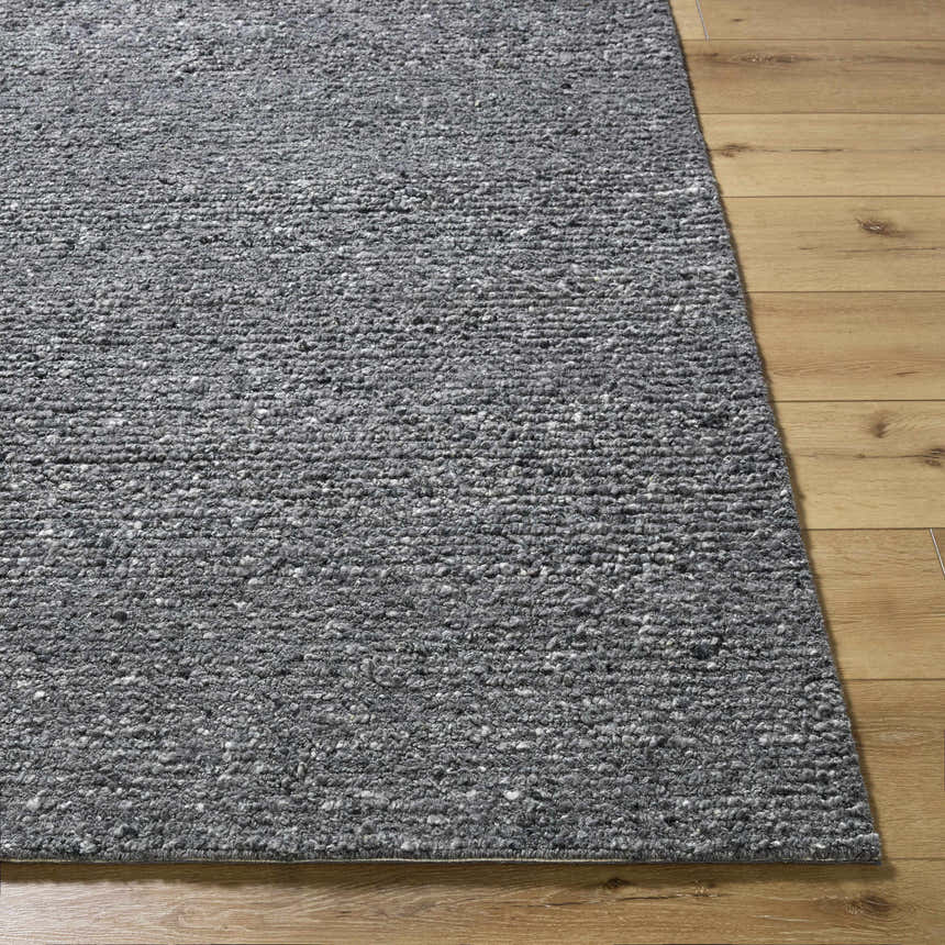 Close-up of the hand-tufted Winta Black Wool Area Rug showing gray tones and textured wool on wood floors. Front