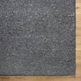 Close-up of the hand-tufted Winta Black Wool Area Rug, showing its gray tones and nubby texture on a light wood floor. Corner