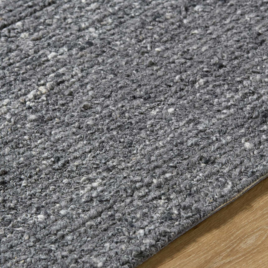 Close up of the hand-tufted Winta Black Wool Area Rug, showing gray tones and textured wool fibers. Texture