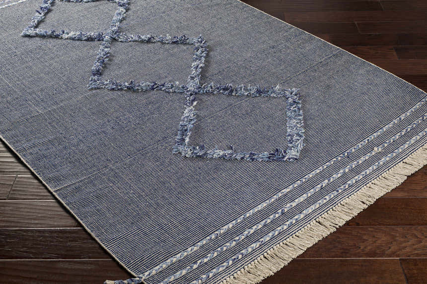 Close-up of the Lavington Carpet, a hand-woven rug in dark blue with denim square patterns and a light beige fringe. Corner