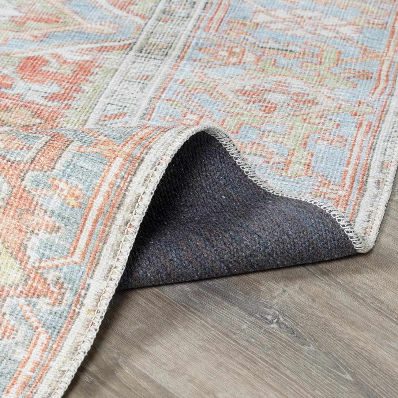 Close-up of the Rust Maayon Washable Rug showing its brick red, blue, and sage traditional pattern and durable backing. Fold