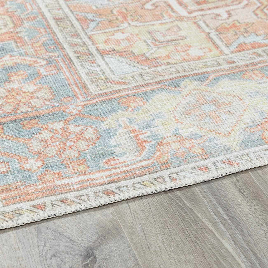 Close-up of the Rust Maayon Washable Rug showing its brick red, blue, and light olive traditional pattern and woven texture. Corner