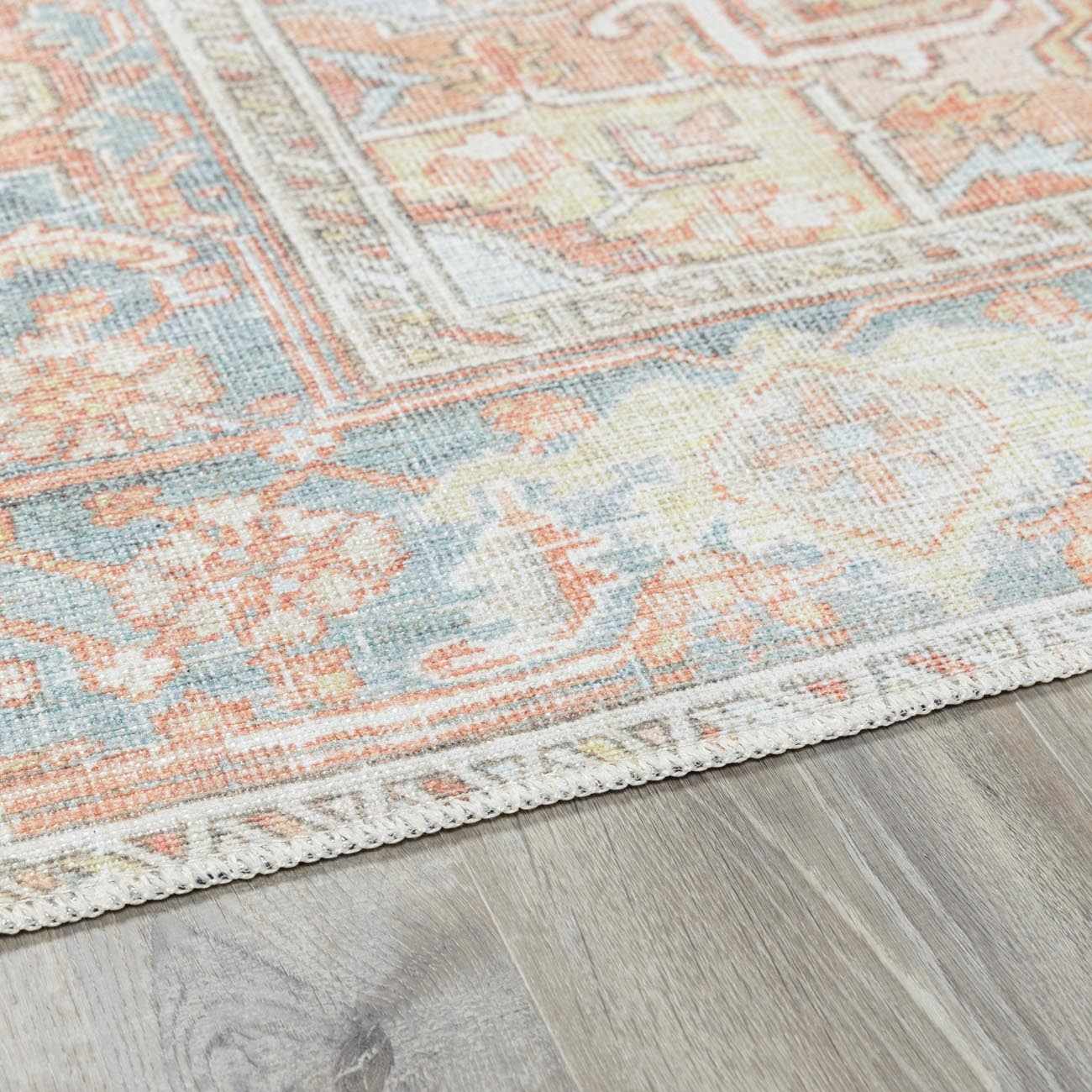 Close-up of the Rust Maayon Washable Rug showing its brick red, blue, and light olive traditional pattern and woven texture. Corner