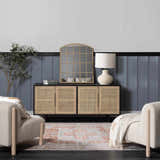Living room scene with a Rust Maayon Washable Rug, beige chairs, and a rattan cabinet against a blue wall. Roomscene-Rectangle