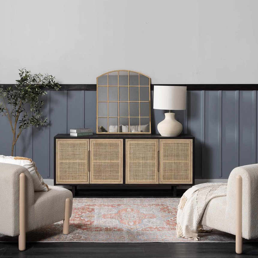 Living room scene with a Rust Maayon Washable Rug, beige chairs, and a rattan cabinet against a blue wall. Roomscene-Rectangle