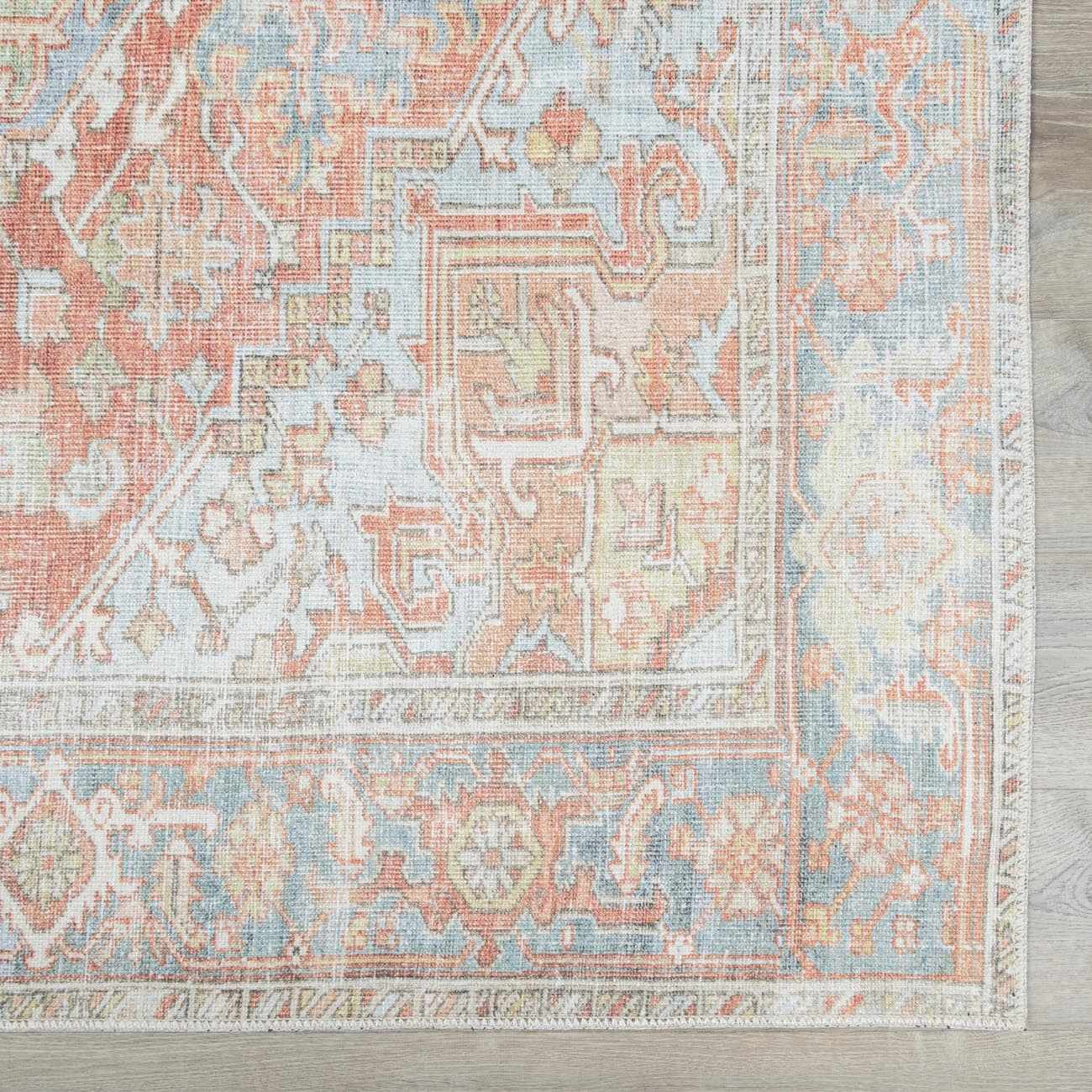 Close-up of the Rust Maayon Washable Rug. Features a traditional, vintage pattern in brick red, brown, and denim blue hues. Swatch