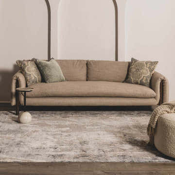 Living room scene with a Maddington Gray Marble Thick Luxe Rug, beige sofa, side table and ottoman. Roomscene-Rectangle