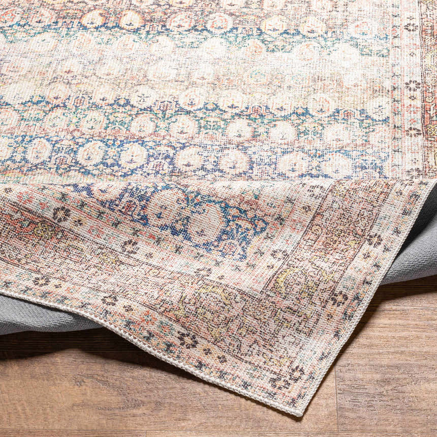 Close-up of the Maligaya Distressed Washable Rug. Bone, dark gray, and nutmeg colors in a Persian-inspired, vintage pattern. Fold
