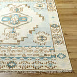Close-up of the McColl Hand Knotted Wool Blend Rug. Features a geometric pattern in cream, brown, and teal on a wooden floor. Front
