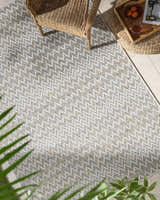 Outdoor patio scene with a wicker chair and Alazne Ivory Area Rug featuring a geometric chevron pattern. Roomscene-Rectangle