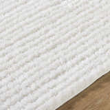 Close-up of the white Alysha Area Rug, a soft shag rug with a subtle striped pattern on a wood floor. Texture