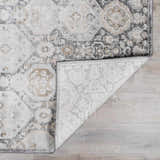 Close-up of the Minoa Area Rug featuring a beige, black, and gray bohemian pattern with a folded corner showing the rug's backing. Fold