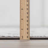 Close-up of the Minoa Area Rug's thickness, showing gray color and machine-woven construction. Pile